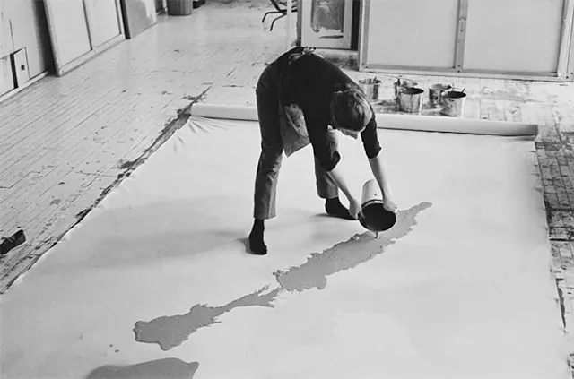 Helen Frankenthaler verse la peinture sur une grande toile non apprêtée en utilisant la technique Soak-Stain.